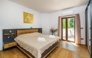 Una camera da letto con un letto, comodini, un climatizzatore a muro, una porta vetrata scorrevole verso un balcone e un quadro giallo appeso alla parete.