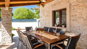 An outdoor dining area with a wooden table and chairs, stone walls, and a view of greenery. - Stunning home in Sajini (Sajini)