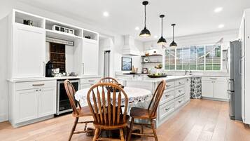 Une cuisine moderne avec des meubles blancs, un îlot central et des luminaires suspendus.