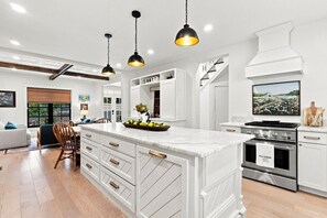 Una cocina moderna con armarios blancos, una isla grande, electrodomésticos de acero inoxidable e iluminación colgante.