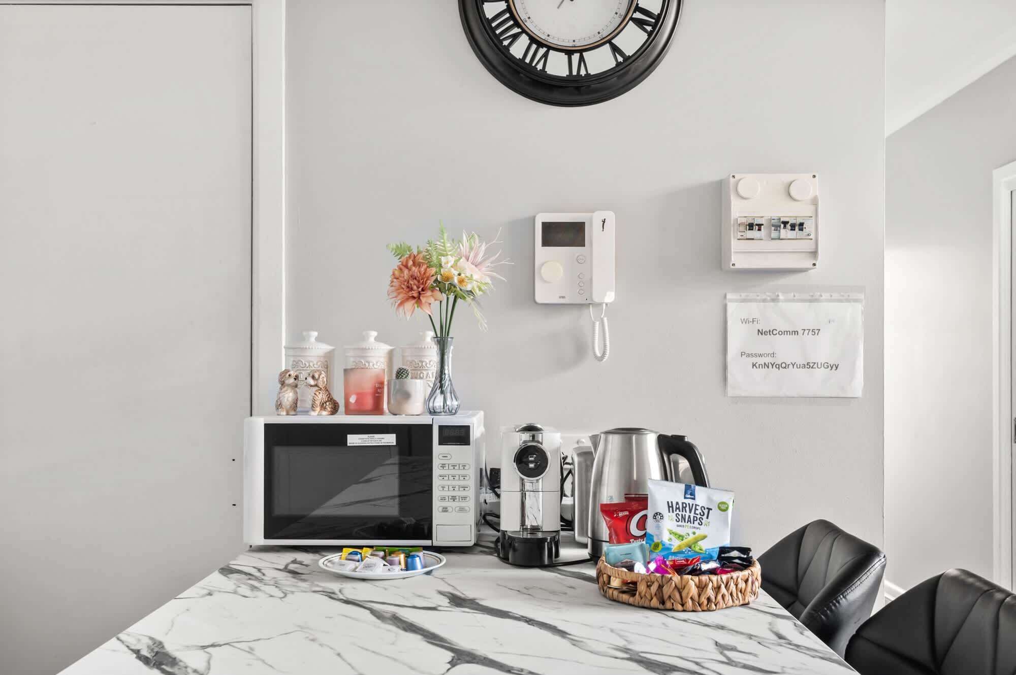 Een moderne keuken met een magnetron, koffiezetapparaat en een mand met snacks op het aanrecht.