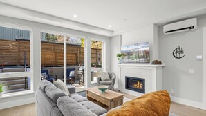 A modern living room with a fireplace, large windows, and a comfortable seating area. - Cordova Bay Living (Victoria)
