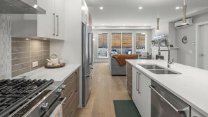A modern kitchen with a gas stove, stainless steel appliances, and a large island with a sink. - Cordova Bay Living (Victoria)