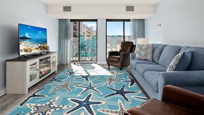 Et moderne hotelværelse med balkon, stort fladskærms-tv, sofa og et tæppe med stjernefisk-motiv.