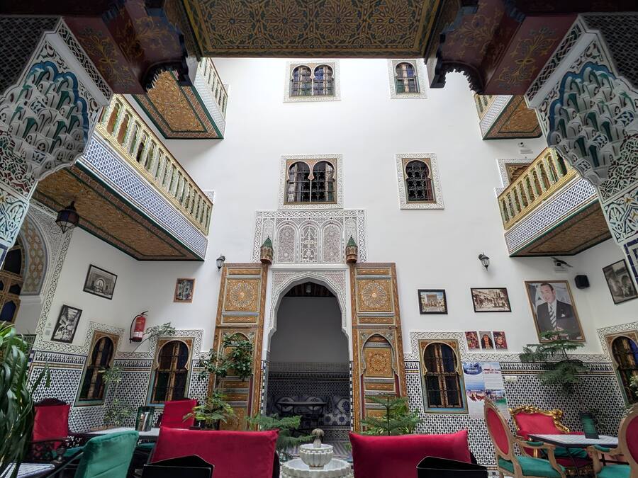 An interior courtyard with intricate tile work, a central fountain, and seating areas with red cushions.