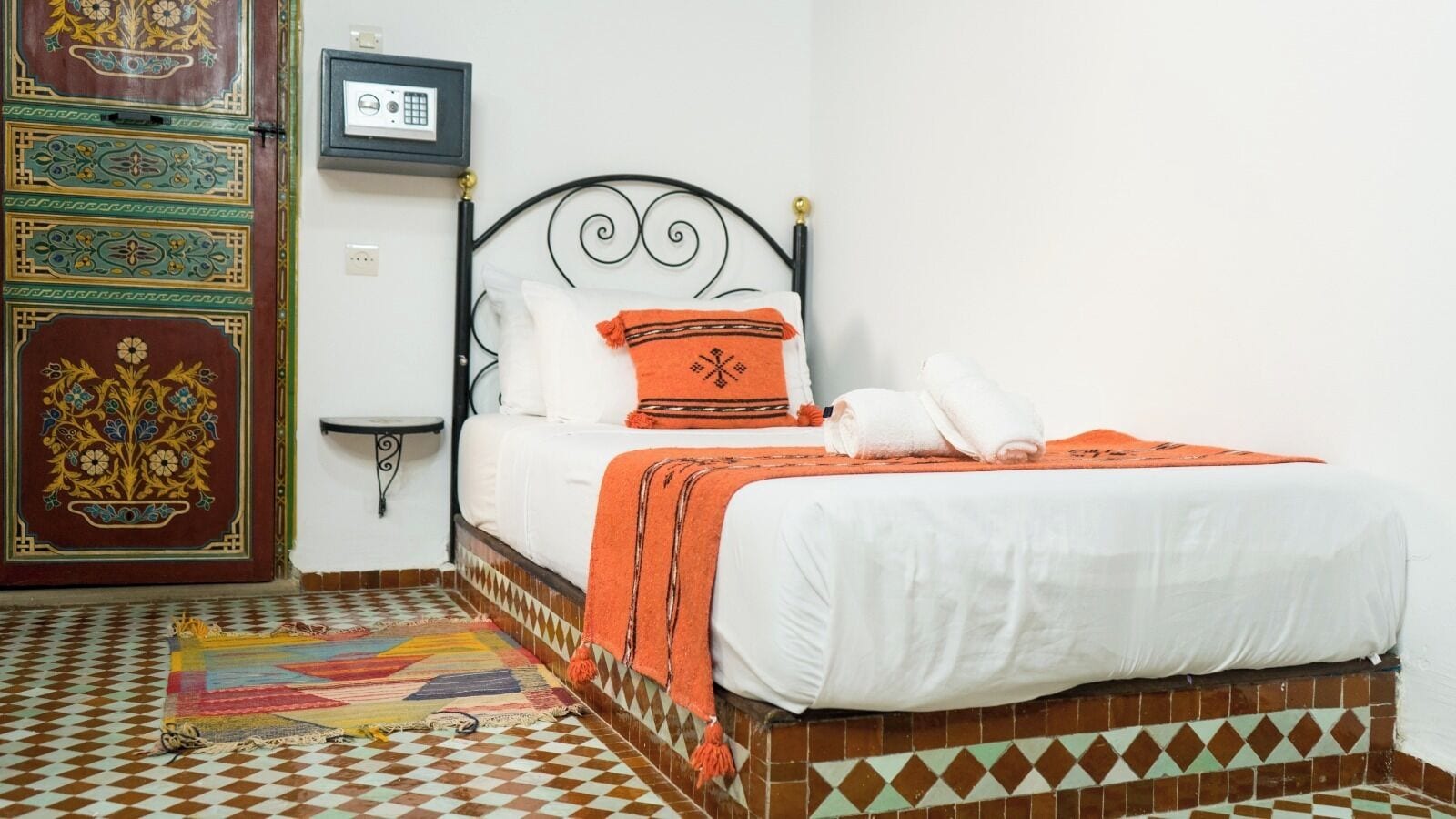 A room with a bed, a patterned rug, a decorative door, and a wall-mounted radio.