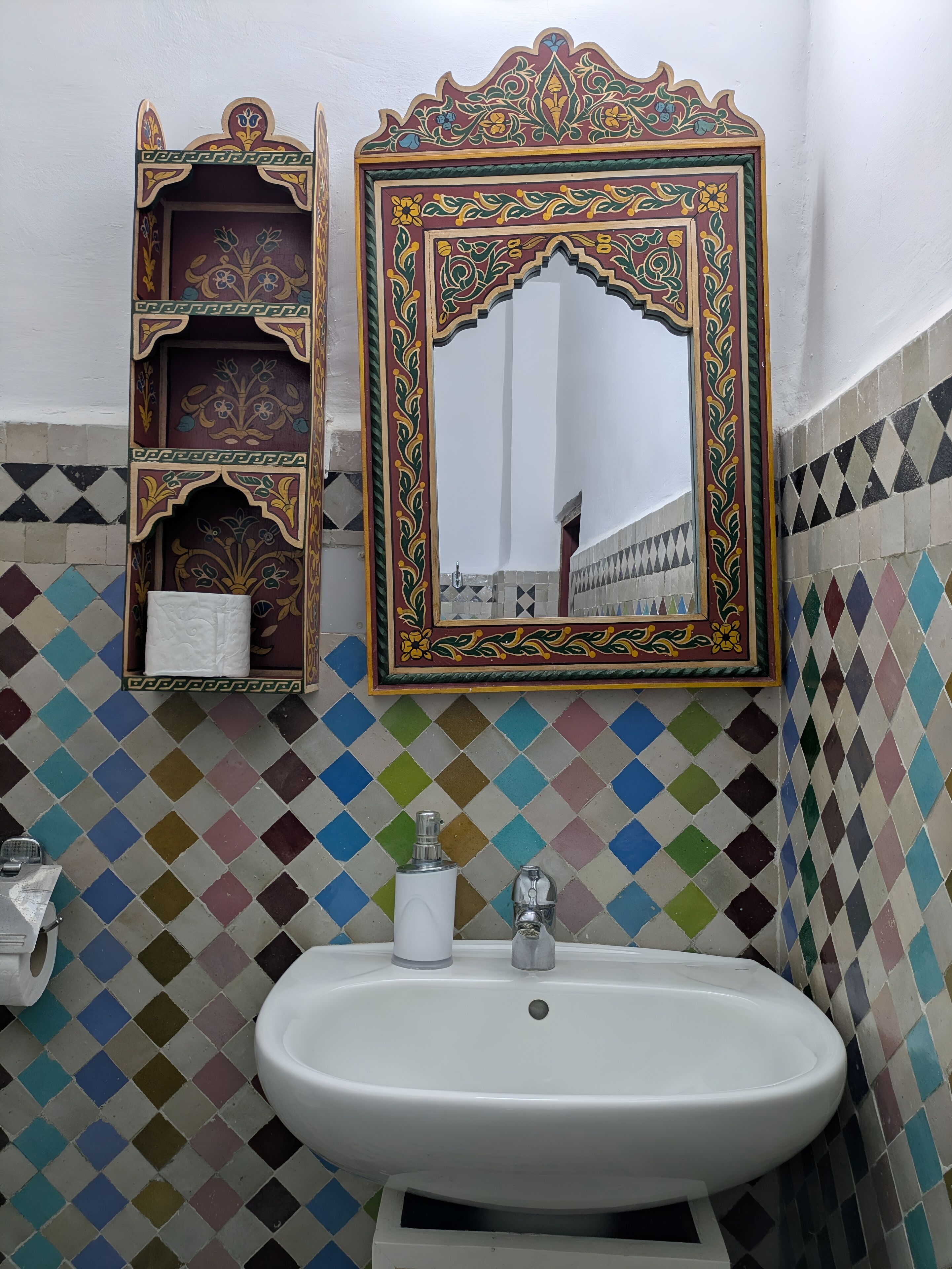 A bathroom with a white sink, a mirror with ornate frame, and a tiled wall with a diamond pattern.