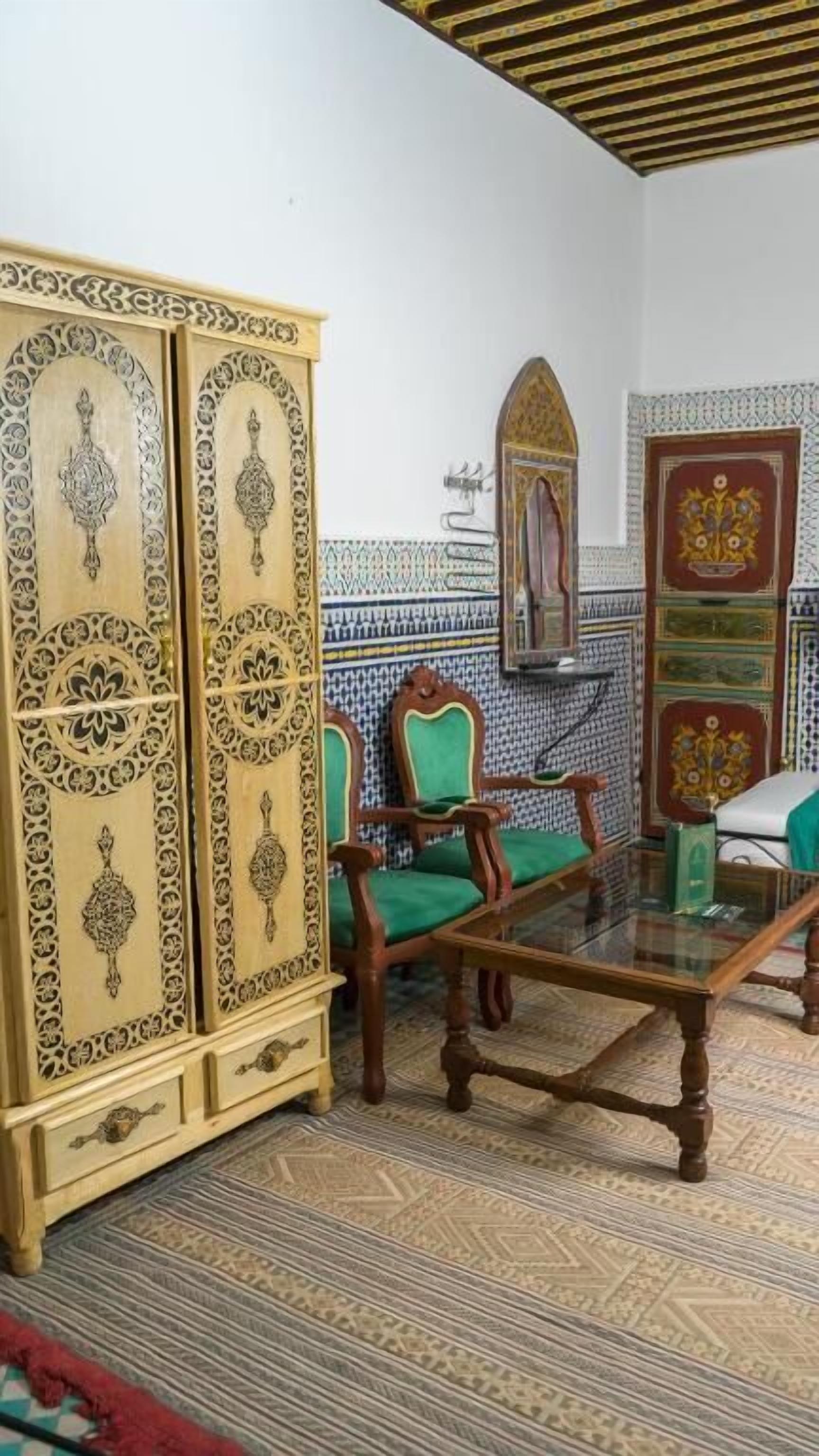 A room with a patterned floor, a green upholstered sofa, a wooden coffee table, and a large cabinet with intricate designs.