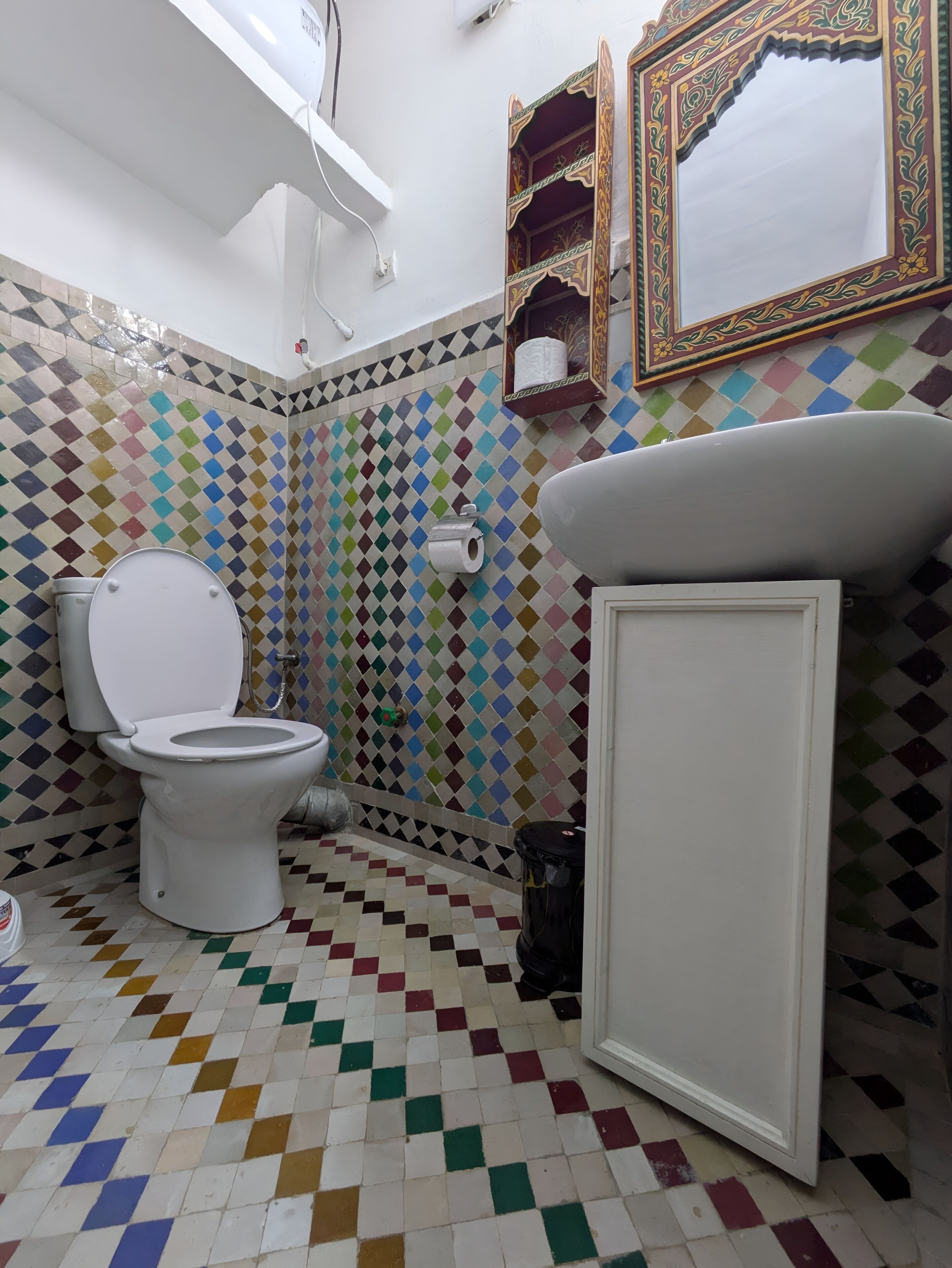 Un bagno con un water bianco, un lavandino e uno specchio. Le pareti sono rivestite di piastrelle con un motivo a rombi colorati.