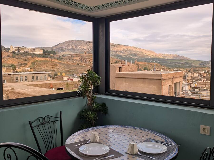 Un balcon avec une table et des chaises, donnant sur un paysage urbain avec des bâtiments et des collines.