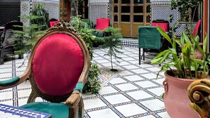Un intérieur marocain traditionnel, avec des sols carrelés, des meubles richement décorés et un balcon aux motifs complexes.