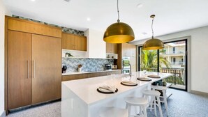 Une cuisine moderne avec des meubles en bois, un îlot en marbre, des tabourets de bar blancs et des luminaires suspendus.