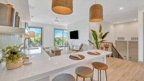 Une cuisine moderne dotée d’un îlot central, de luminaires suspendus et offrant une vue sur l’extérieur.