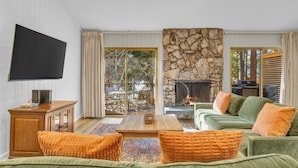 A spacious living room with a stone fireplace, green sofas, and a flat-screen TV mounted on the wall. - King's Beach condo with stunning views! (Kings Beach)