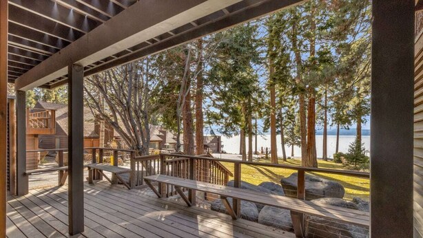A wooden deck with benches and a railing overlooking a beach with trees and a body of water. - King's Beach condo with stunning views! (Kings Beach)
