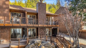 A two-story log cabin with a balcony, large windows, and a stone fireplace. - King's Beach condo with stunning views! (Kings Beach)
