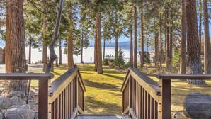 A wooden deck leading to a grassy area with tall trees and a lake view. - King's Beach condo with stunning views! (Kings Beach)