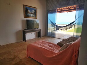 Ein Schlafzimmer mit einem Bett, einem Fernseher auf einem Schrank und Blick auf einen Strand durch eine Glastür.