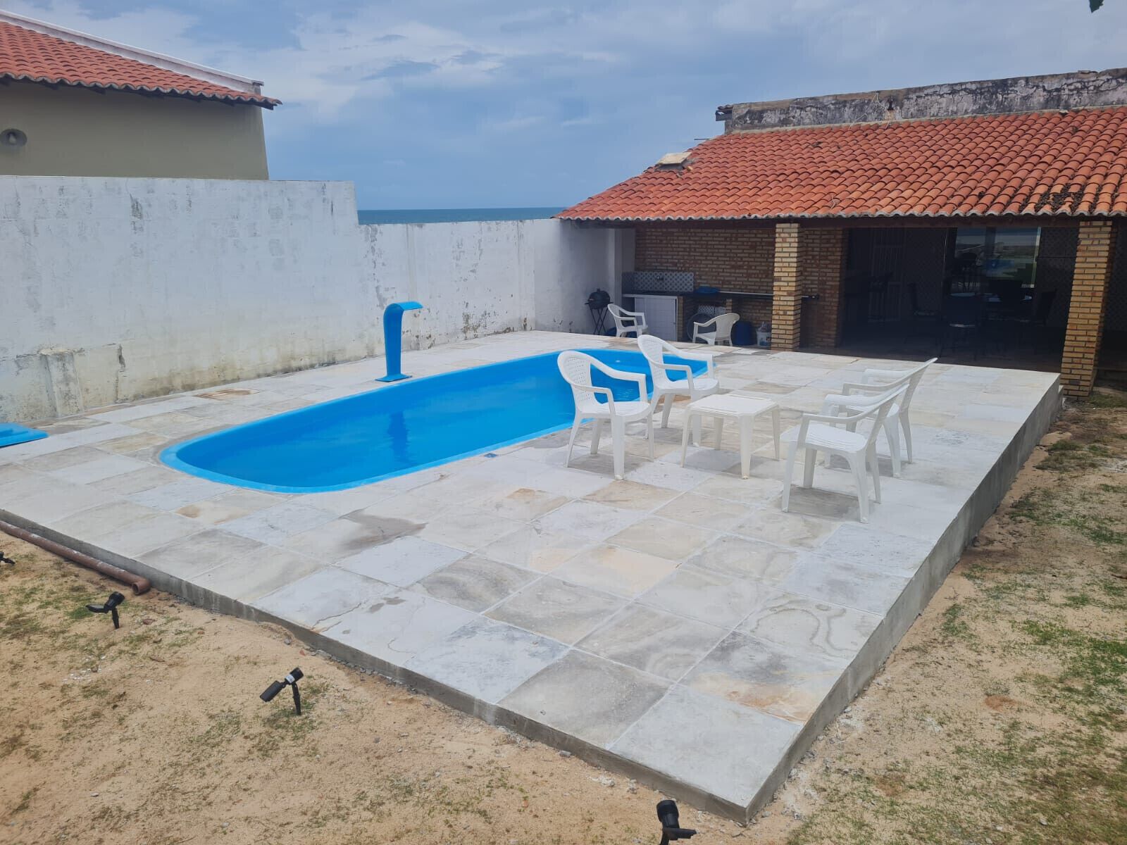 Une piscine entourée d’une terrasse en béton, avec des chaises blanches et une table.
