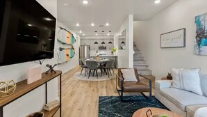 Un salon moderne doté d’un téléviseur à écran plat, d’un coin repas avec une table ronde et d’un escalier menant à un autre niveau.