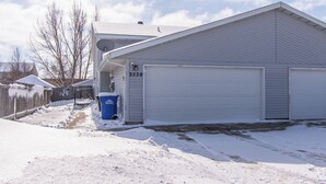 Un edificio a un piano con un garage, un bidone blu per la raccolta differenziata e un cortile coperto di neve.