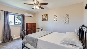 A bedroom with a bed, a ceiling fan, an air conditioning unit, a dresser, and decorative wall art. - The Country Farmhouse (Platteville)
