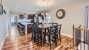 A spacious kitchen with wooden flooring, a dining area with a large table and chairs, and a modern chandelier. - The Country Farmhouse (Platteville)
