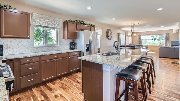 A modern kitchen with a central island, wooden flooring, and a dining area with a view. - The Country Farmhouse (Platteville)