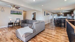 A spacious living area with a grey sectional sofa, a small side table, and a ceiling fan. A dining area with a wooden table and chairs is visible in the background. - The Country Farmhouse (Platteville)