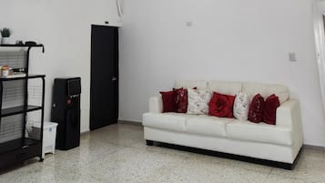 Un salon avec un canapé blanc, des coussins rouges et blancs, un meuble noir, une petite table et un luminaire au plafond.
