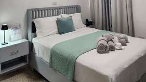A neatly arranged bedroom with a bed, bedside table, lamp, and a wall-mounted air conditioning unit. - Hotel Feliz Estancia (La Romana)