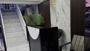 A modern reception area with a marble staircase, a black reception desk, and a seating area with a plant. - Hotel Feliz Estancia (La Romana)