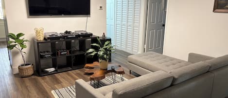 A living room with a grey sofa, a flat-screen TV, a sound system, and a wooden coffee table.