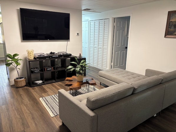 A living room with a grey sofa, a flat-screen TV, a sound system, and a wooden coffee table.