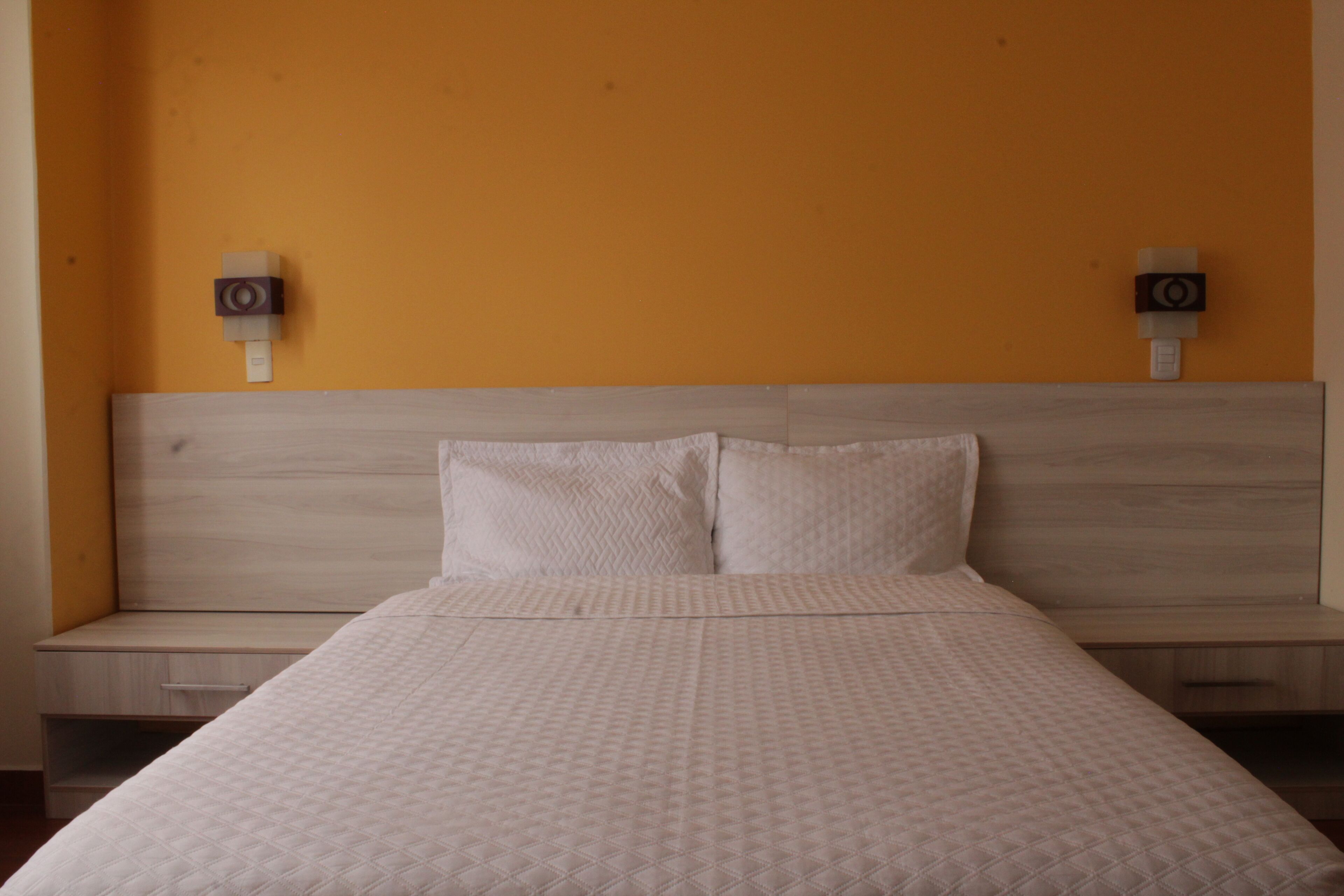 Una habitación de hotel con cama, dos mesitas de noche y altavoces empotrados.