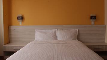 Una habitación de hotel con cama, dos mesitas de noche y altavoces empotrados.