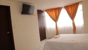 Ein Schlafzimmer mit Bett, einem an der Wand befestigten Fernseher und Vorhängen an den Fenstern.