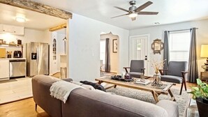 Un salon moderne comprenant un canapé, deux fauteuils, une table basse et un ventilateur de plafond.