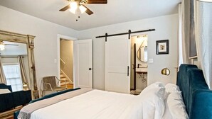 Une chambre d’hôtel comprenant un lit, un ventilateur de plafond, un miroir, une porte et une salle de bain avec un lavabo et un miroir.