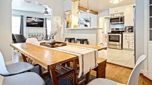 Une cuisine moderne avec des meubles blancs, des appareils en acier inoxydable et une table à manger en bois, accompagnée de chaises.