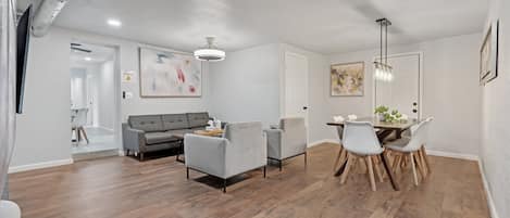 Una sala de estar moderna con un sofá gris, dos sillones, una mesa de comedor con sillas y una lámpara en el techo.