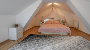 A bedroom with a sloped ceiling, a bed with pink bedding, a white bedside table, a small dresser, and a fluffy rug. - La Lukas - MUSSY SUR SEINE (MUSSY SUR SEINE)