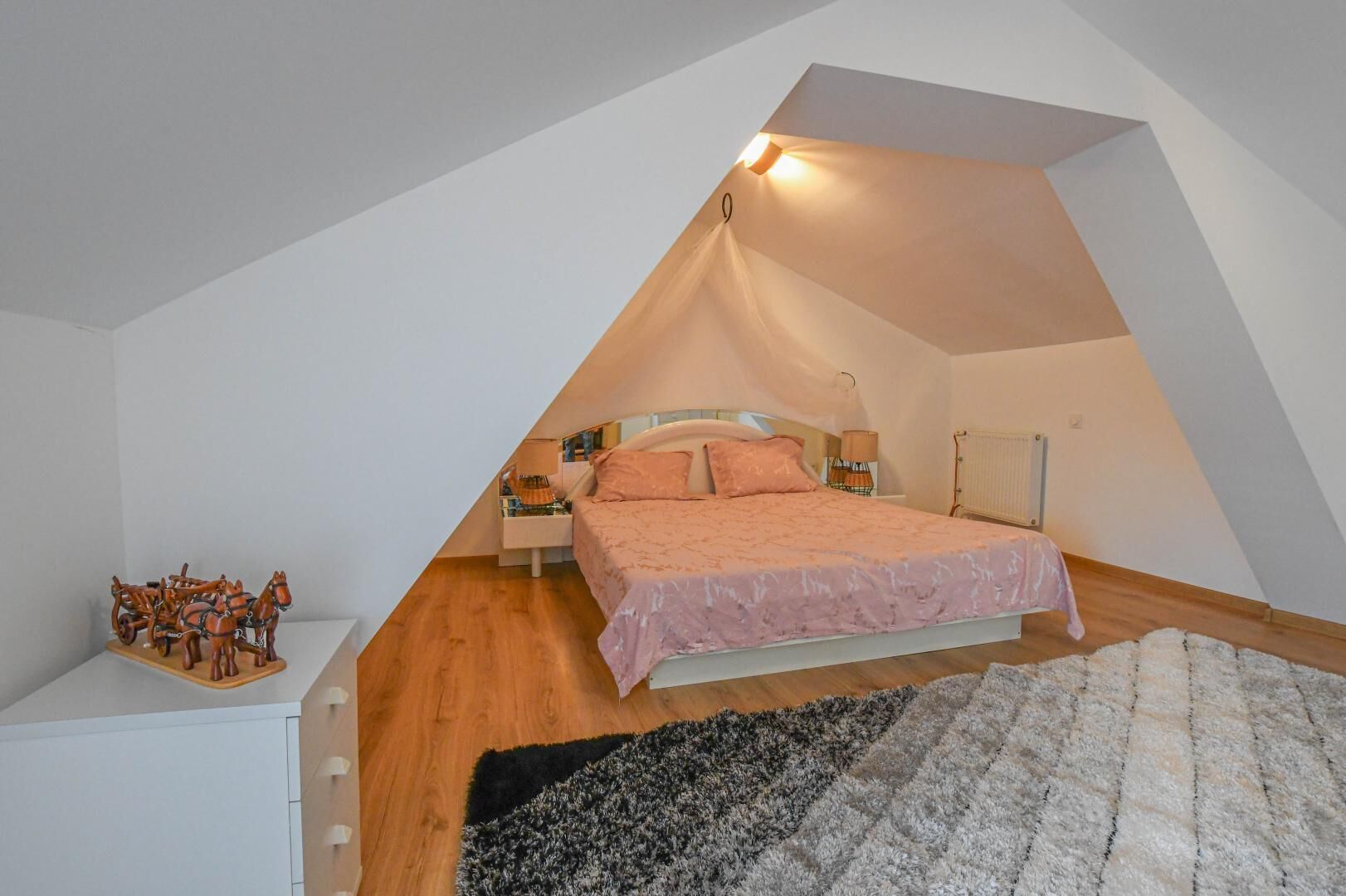 Ein schräges Schlafzimmer im Dachgeschoss mit einem Bett, Nachttischen und einem kleinen Holztisch.