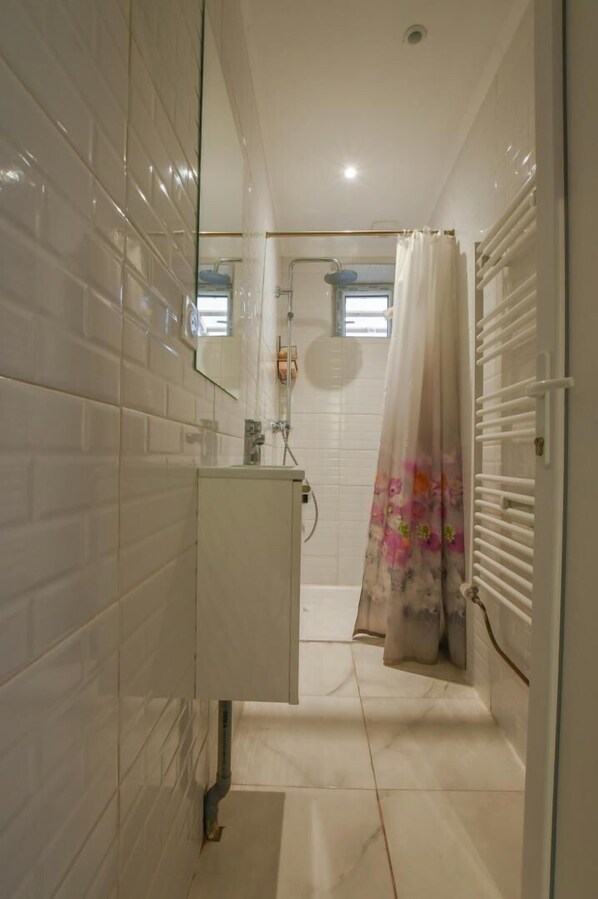 A bathroom with white tiled walls, a white sink, and a shower with a floral curtain.