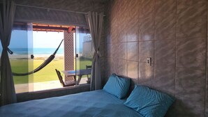 Ein Schlafzimmer mit einem großen Bett, Blick auf den Strand und einer Hängematte davor.