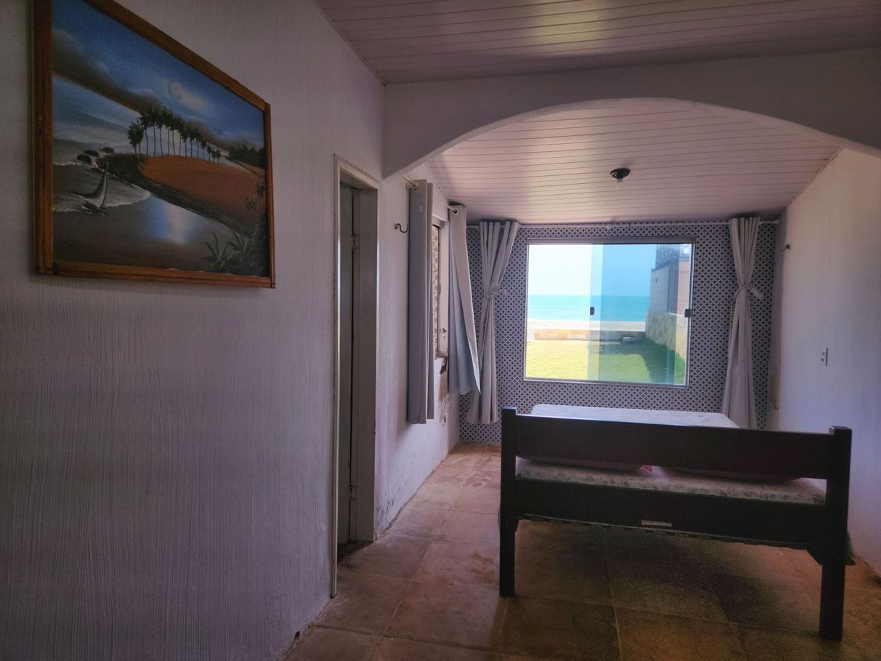 Um corredor com um banco, um quadro e vista para a praia através de uma janela.