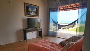 Ein Schlafzimmer mit einem Bett, einem Fernseher auf einem Schrank, einer Hängematte neben einer Glastür und einem Bild an der Wand.