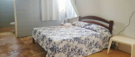 A bedroom with a bed, a bedside table, a mirror, and a shower.
