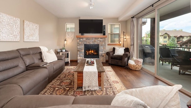 Una sala de estar moderna con chimenea de piedra, televisor de pantalla plana y un amplio ventanal corredizo al exterior.