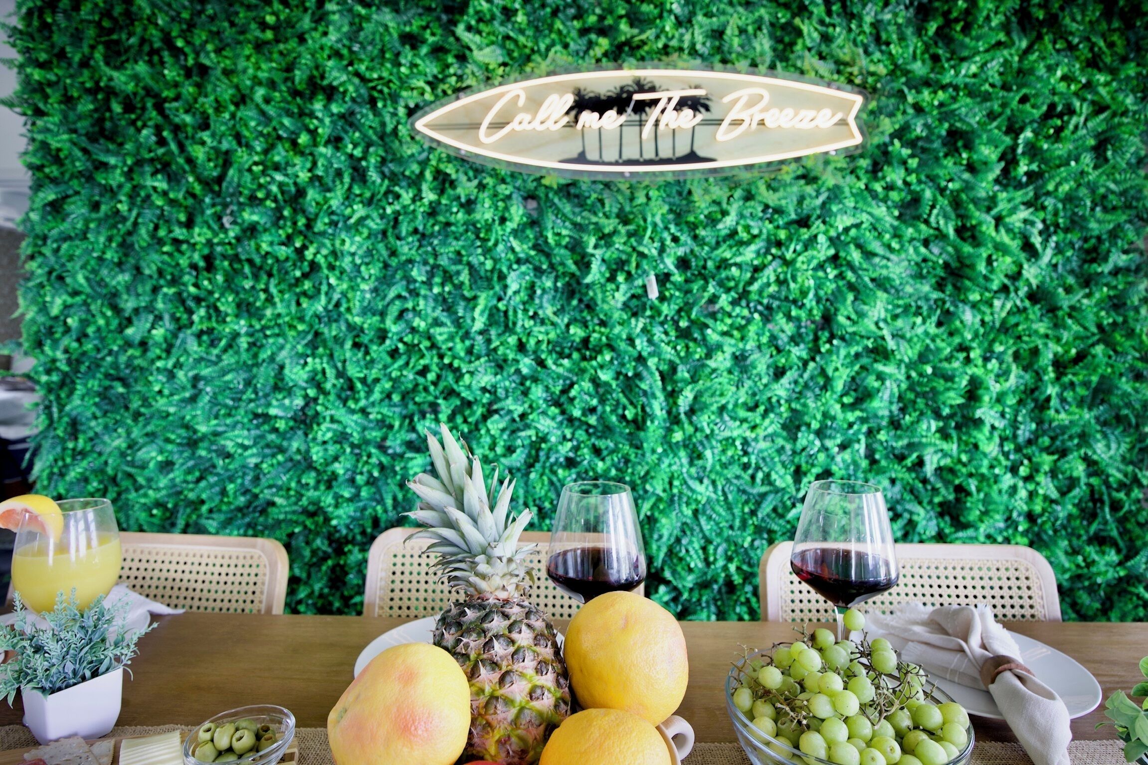 A table set with fruits, glasses of juice and wine, and a sign that reads "Call me The Breeze".